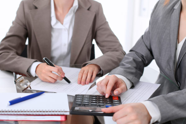 Two female bookkeepers use a calculator as they prepare a client’s financial statements.