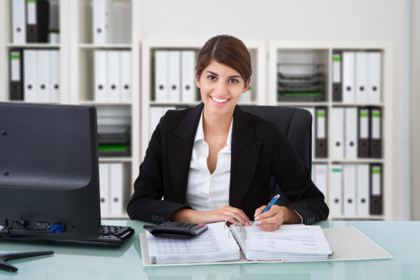 Smiling female accountant prepares a client’s financial statements at her desk.