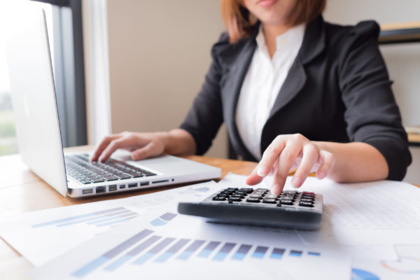 Asian female accountant working at her computer makes calculations with a calculator.