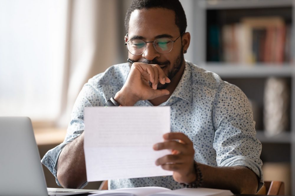 African man sitting at desk reading letter feels satisfied